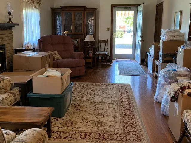 Older living room partway through an estate cleanout with boxes stacked and bagged linens by the door