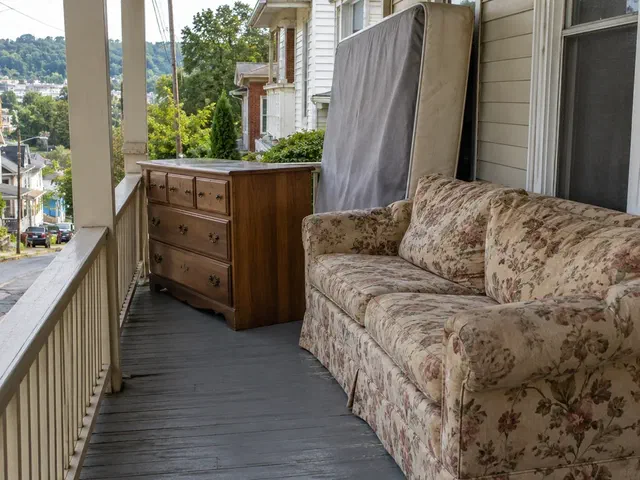 Floral sofa, wooden dresser, and box spring waiting on a covered front porch in Clarksburg