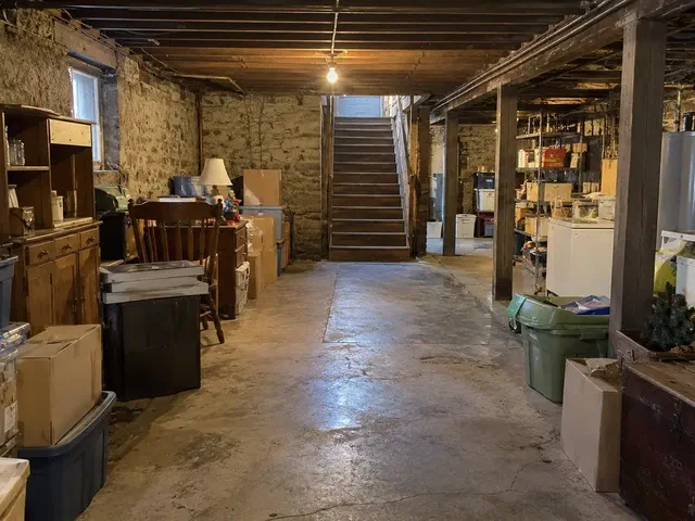 Cluttered stone-wall basement partway through a cleanout with a cleared path to the stairs